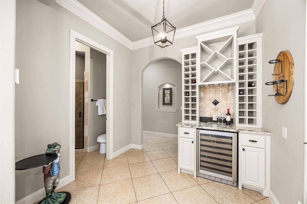 A charming Wine Bar, located just off the Family Room and Kitchen area, features a beverage refrigerator, granite countertop, wine racks, and an under-cabinet wine glass hanger—perfect for entertaining and enjoying your favorite vintages in style.  Just across the hall, a full guest Bath or pool Bath provides convenience and comfort for visitors, featuring elegant finishes and thoughtful design. A sophisticated birdcage chandelier and crown molding add a touch of elegance to the space.