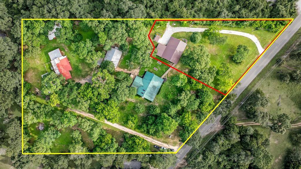 This aerial photo shows 4 acres of a lush property with home 1 outlined in red, home 2 the log home and building 3 plus 2 additional outbuildings. The property features a mix of open spaces and wooded areas, providing a private and serene setting. A curved driveway leads to the log house, and the property is bordered by woods and offers easy access to the 99, 249 Magnolia and the Exxon Campus.