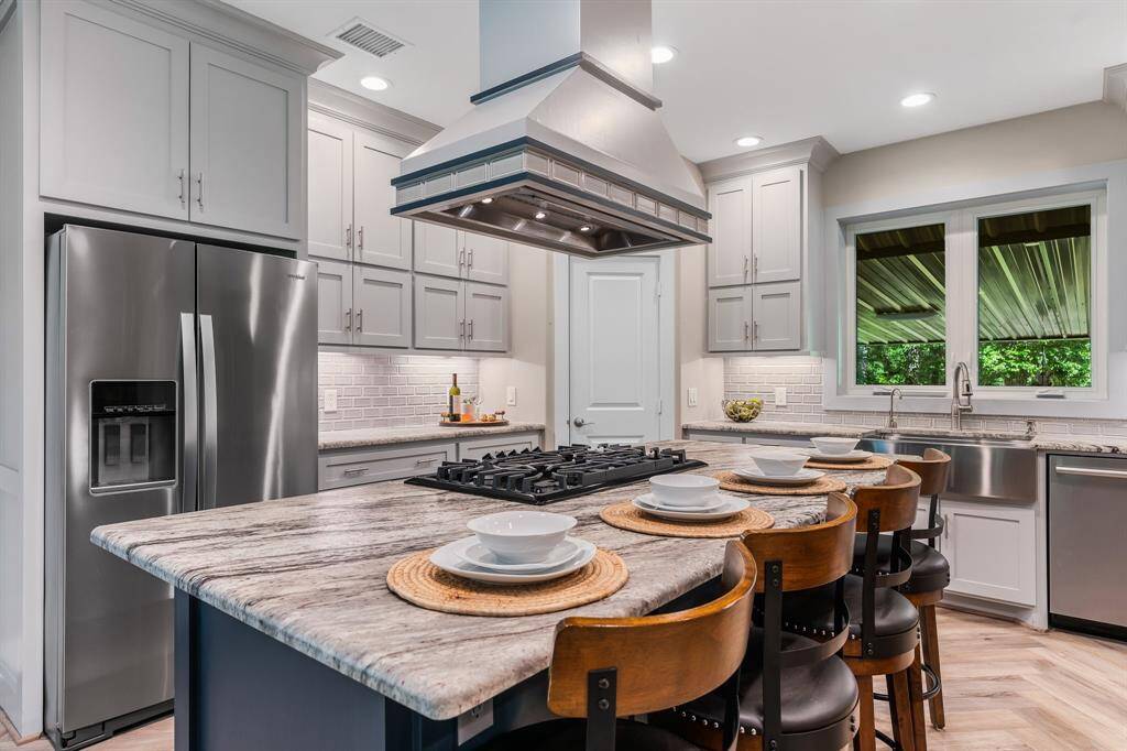 This modern kitchen features stainless steel appliances, white cabinetry, subway tile backsplash, and a central island with leathered granite counters, breakfast bar seating, all under bright recessed lighting.