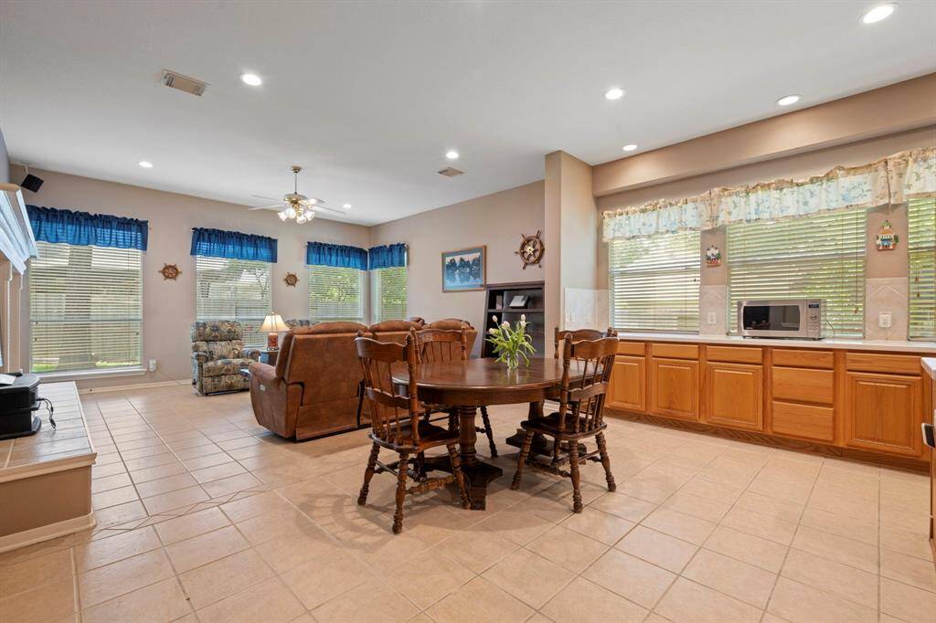 This spacious, open-concept living area features tiled flooring, large windows with plenty of natural light, and a cozy seating area. The kitchen has ample counter space and wooden cabinetry, ideal for family gatherings.