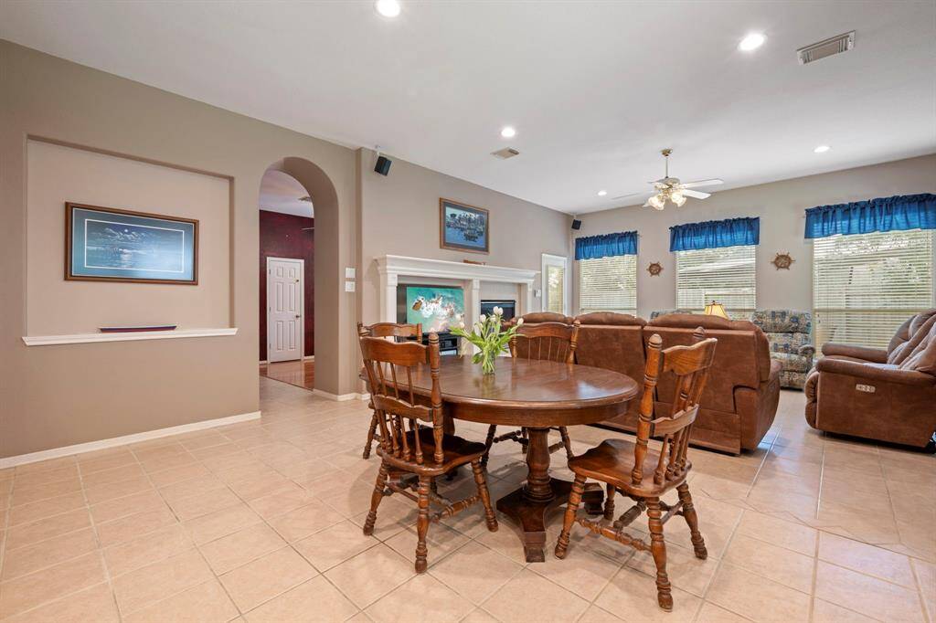 This spacious living area features a cozy fireplace, ample natural light from multiple windows, and an open layout. It includes a comfortable seating arrangement and a dining table, perfect for family gatherings. The neutral tones and tile flooring add a warm, inviting atmosphere.