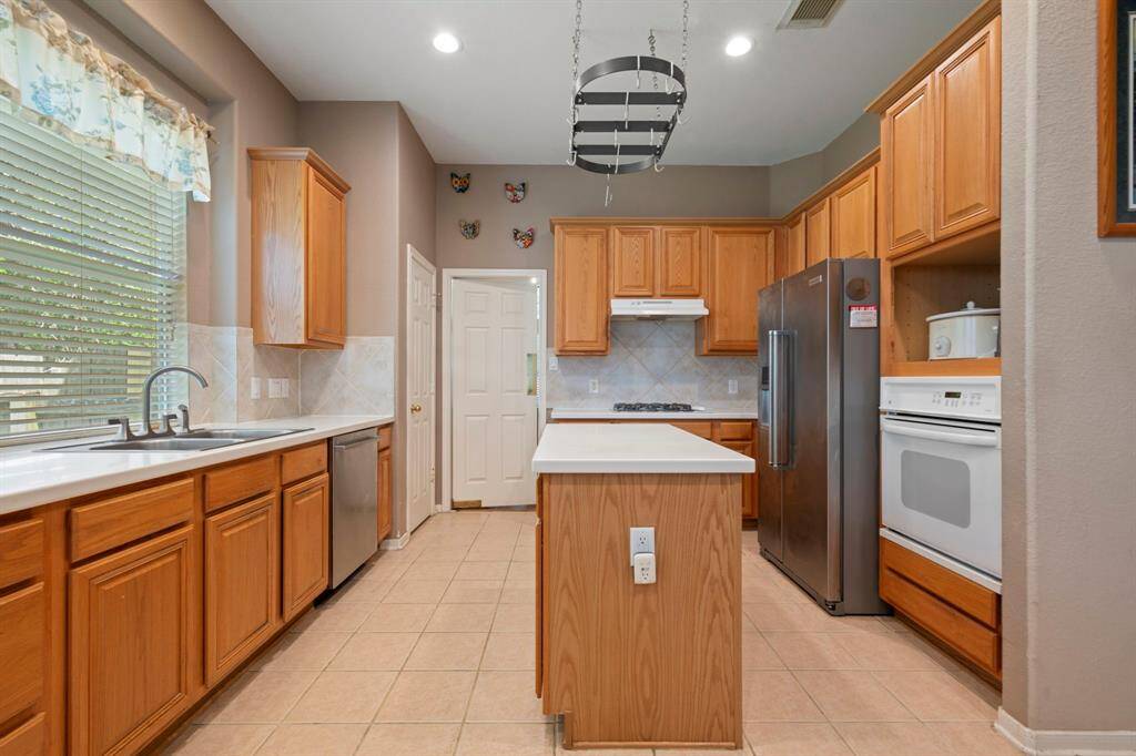 This kitchen features warm wooden cabinets, a central island, gas cooktop & oven, stainless steel Bosch dishwasher & refrigerator. .