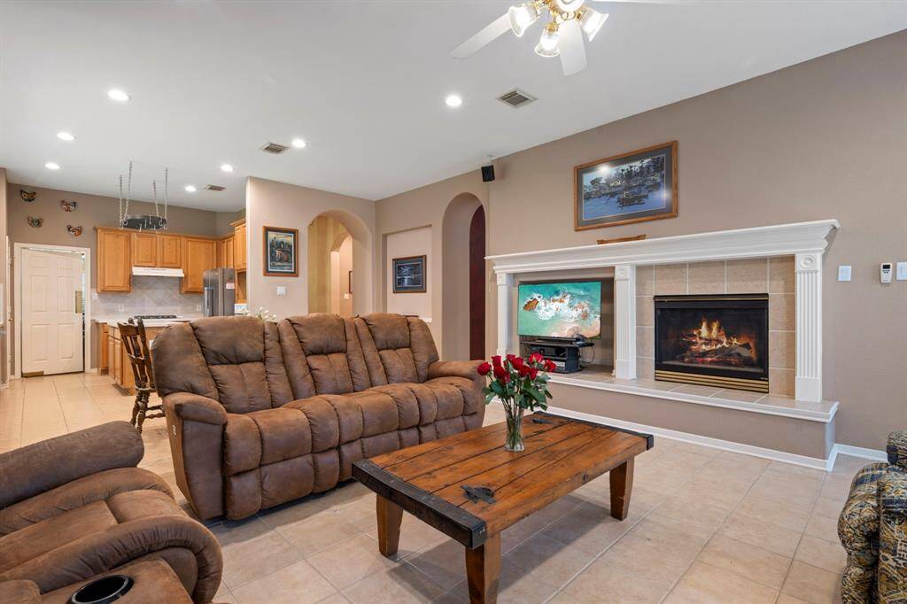 Another view of this inviting living room featuring a cozy fireplace and open layout that seamlessly connects to the kitchen. Warm, neutral tones create a welcoming atmosphere, perfect for relaxation and entertaining.