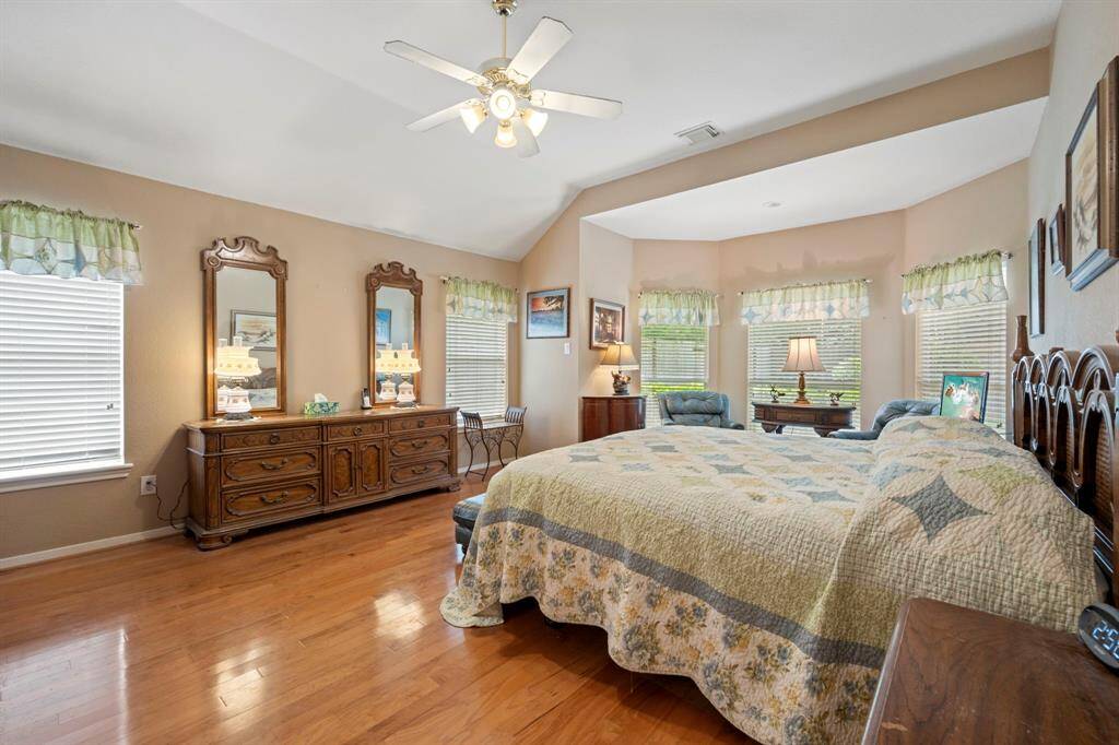 Spacious primary bedroom featuring an elegant bay window, crown molding, abundant natural light, and rich wood floors.