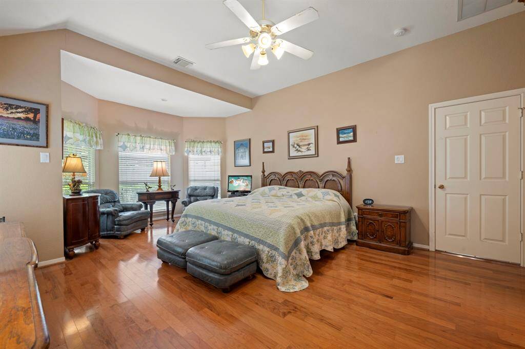 Spacious bedroom with hardwood floors, neutral walls, and a ceiling fan.