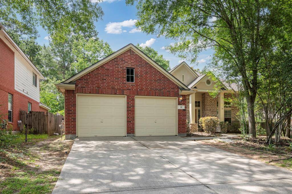 This lovely home features a red brick exterior with a dual garage. Nestled among mature trees, it offers a welcoming front porch and a well-maintained driveway.