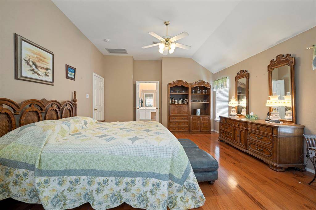 Discover this inviting bedroom featuring elegant hardwood floors, a vaulted ceiling with a fan, abundant natural light, and a convenient ensuite.