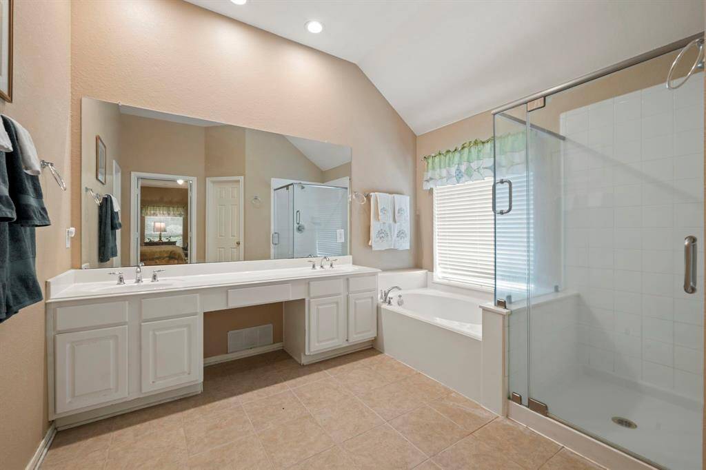 Bright and spacious bathroom with a double vanity, large mirror, glass-enclosed shower, and a separate bathtub. Neutral tiles and soft lighting create a welcoming atmosphere.