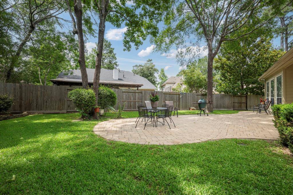 This photo showcases a spacious, well-maintained backyard with a paved patio area perfect for outdoor dining and relaxation. Surrounded by lush greenery and mature trees, it offers privacy and a serene atmosphere.