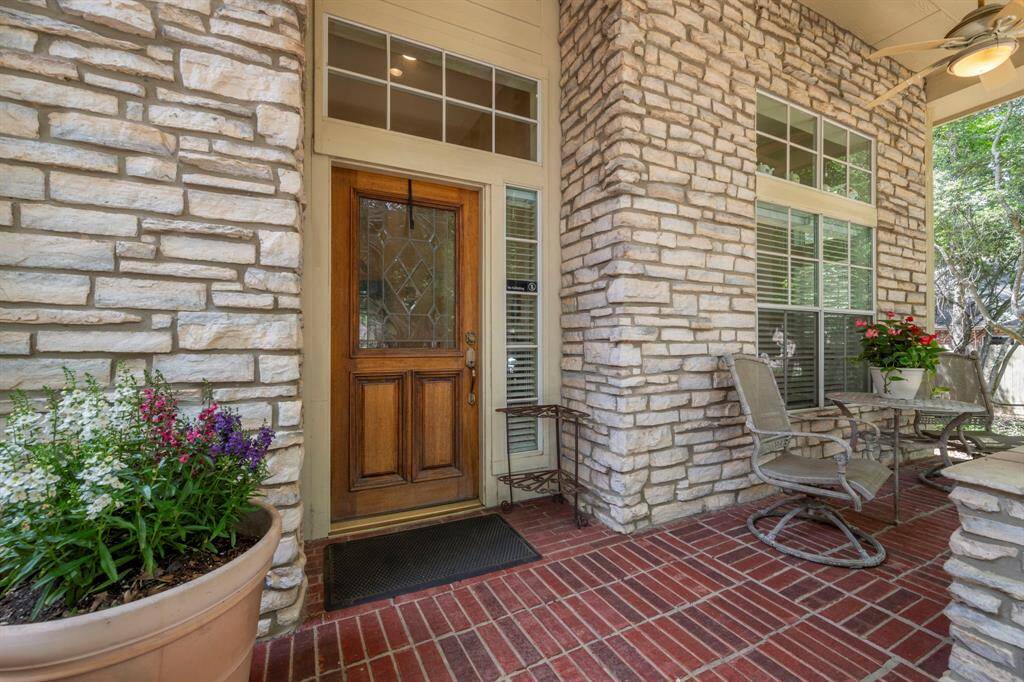 Front porch with stone accent walls, a wooden door with decorative glass, and red brick flooring. Porch provides a nice space for a sitting area for relaxing & enjoying the view or talking with friends or neighbors