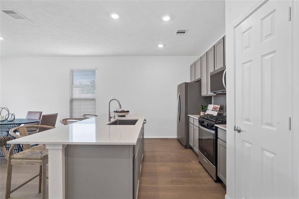 This spacious kitchen features high ceilings, stained wood cabinets, Silestone countertops, SS appliances, modern tile backsplash, recessed lighting, huge kitchen island with single sink and space for breakfast bar, and a pantry all overlooking your huge family room.