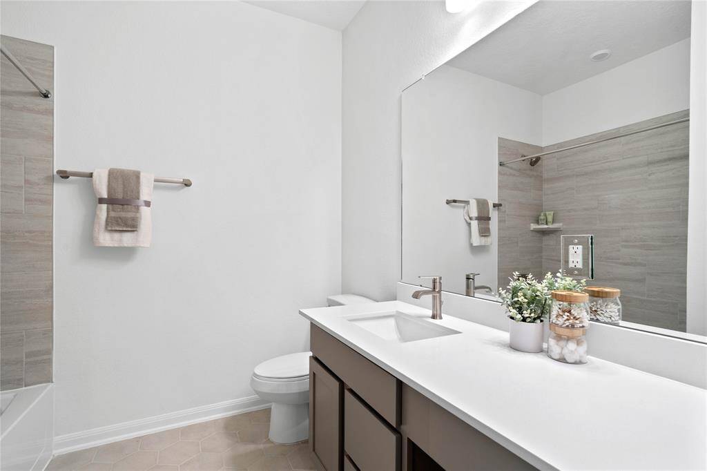 Secondary bath features tile flooring, bath/shower combo with tile surround, stained wood cabinets, beautiful light countertops, mirror, sleek fixtures and modern finishes.