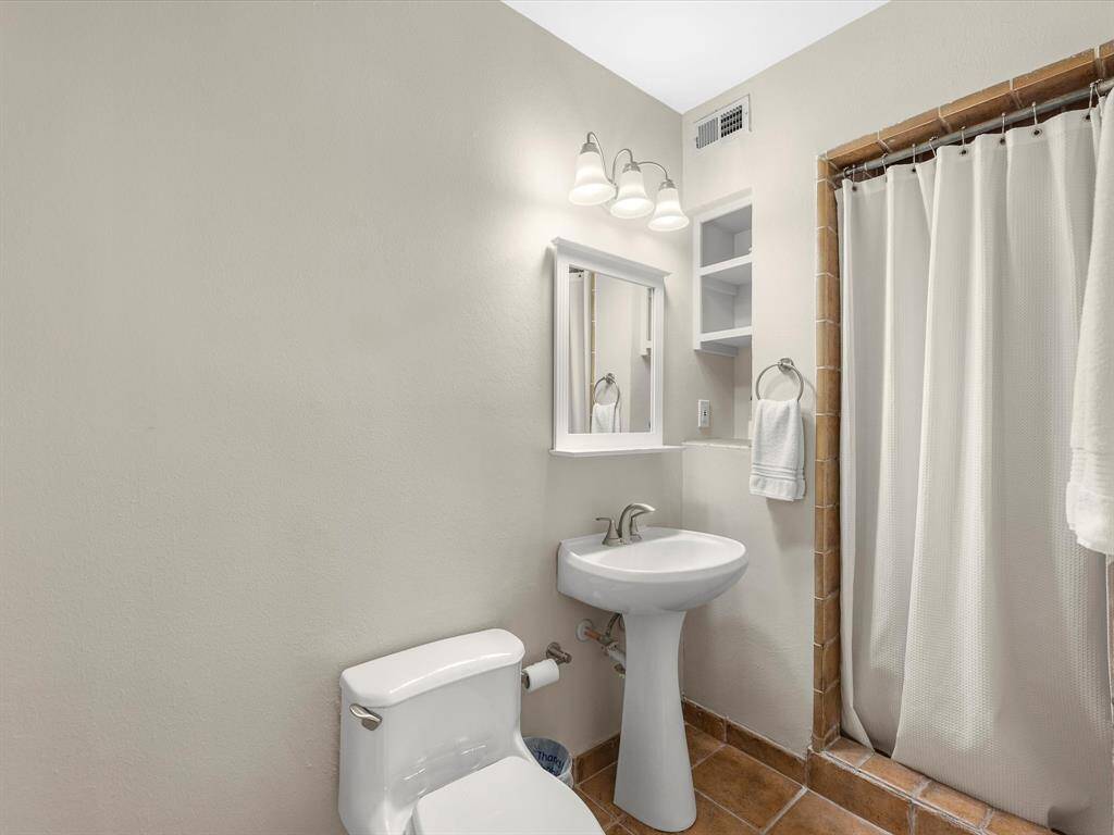 Primary bathroom featuring a modern pedestal sink, warm tiled flooring, and ample natural light for a refreshing start to your day.