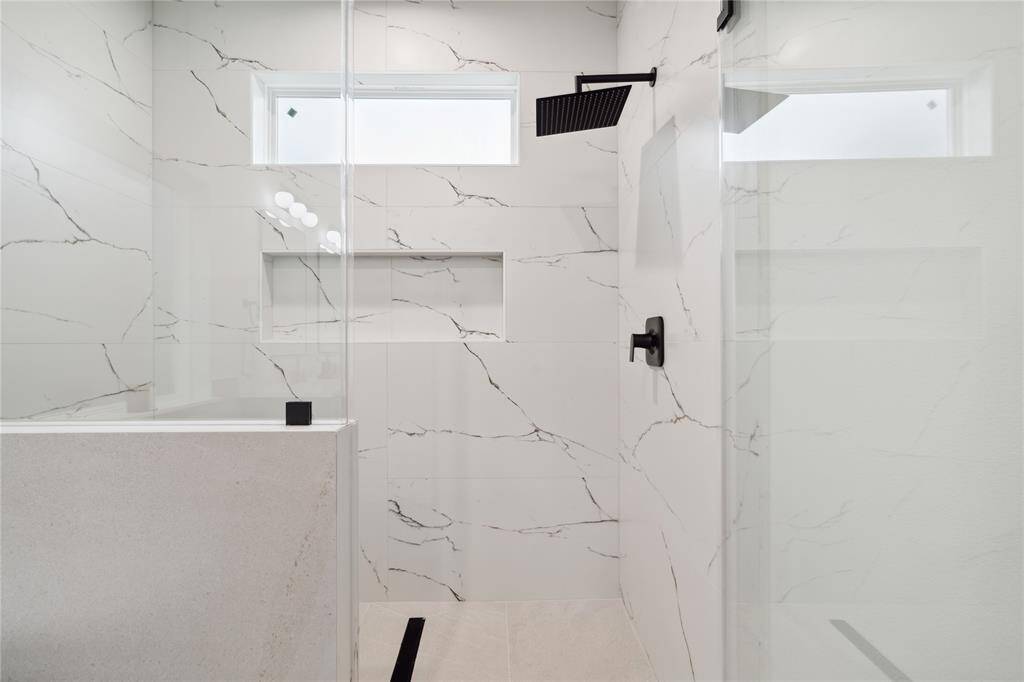 Indulge in a spa-like experience with this stunning walk-in shower, adorned with elegant white tiles, an oversized shampoo niche, and a built-in bench for ultimate comfort