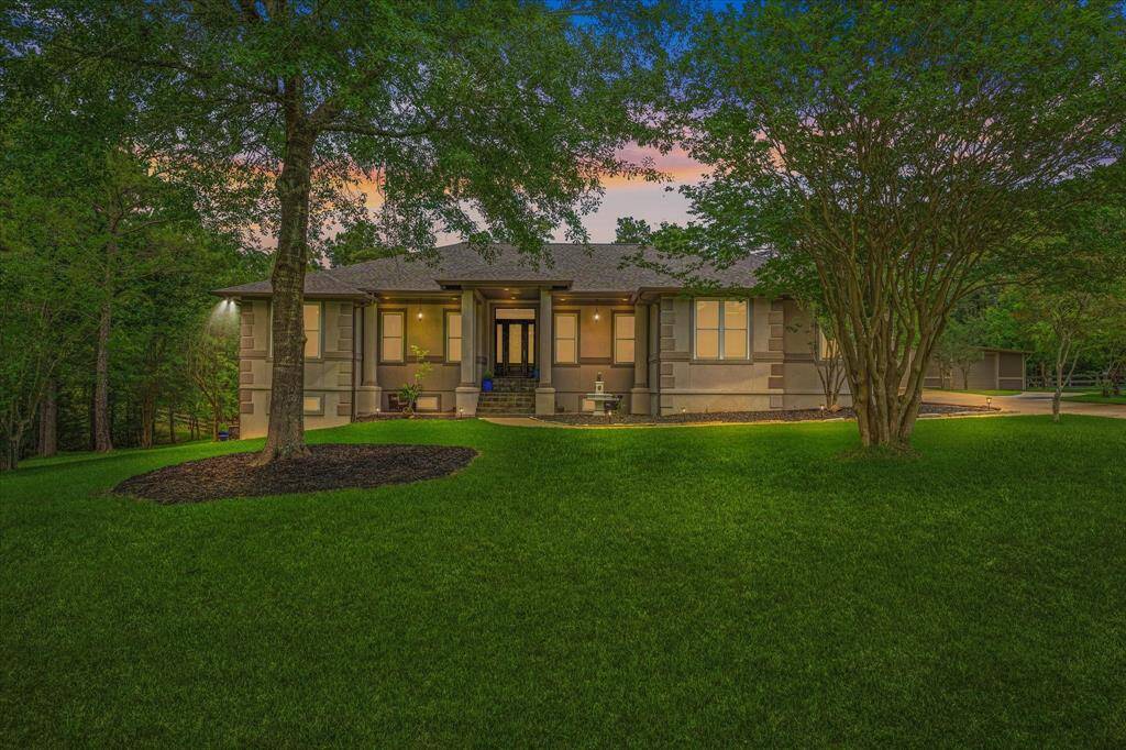 This photo showcases a charming home with full walk out basement is surrounded by lush greenery and mature trees. The house features a welcoming entrance, well-manicured lawn, and a serene, wooded backdrop, perfect for privacy and nature lovers.