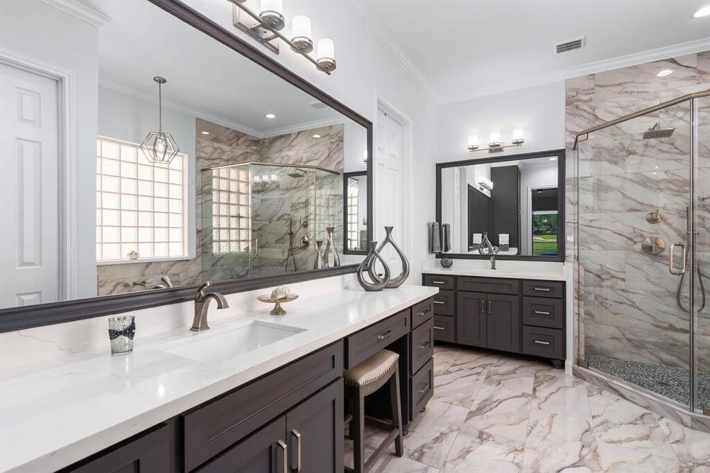 This stunning, ensuite bath has been completely remodeled with double vanities, custom cabinetry, expansive framed mirrors, quartz countertops and designer lighting.