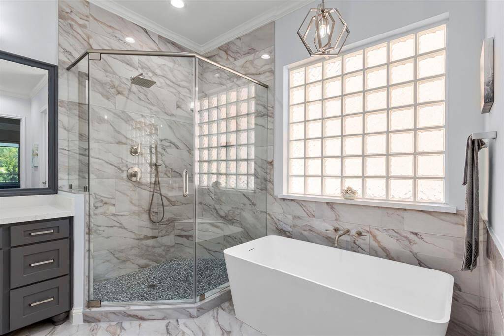 Gorgeous spa-like bath boasts porcelain tile floors and walls, a modern rectangular freestanding tub and glass-enclosed shower. The large glass-block window offers privacy while filling the space with beautiful natural light.