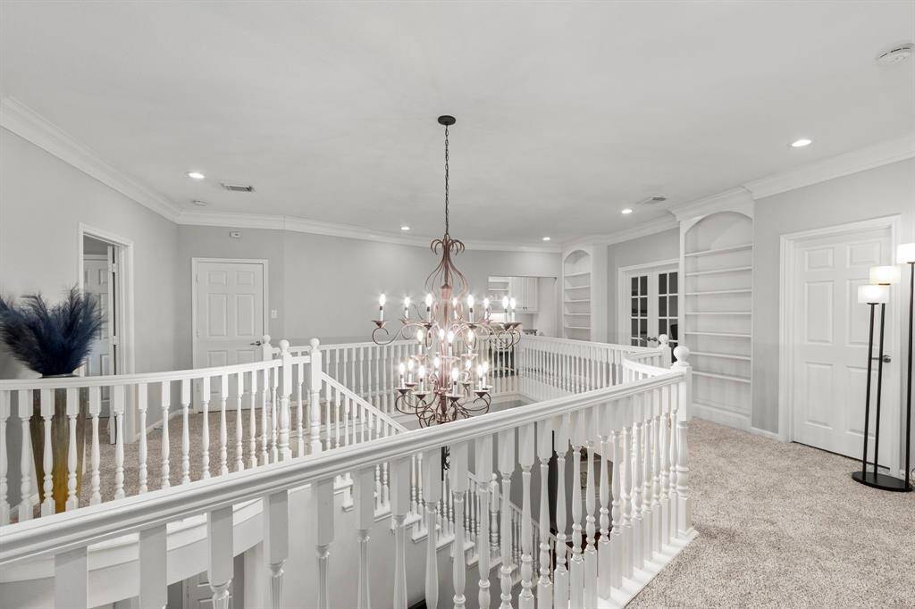 The upstairs area is spacious and the hallway offers wonderful custom built-in shelving that surrounds the gameroom. The closed door across the stairway in this picture opens to a very large, floored attic space for fabulous storage options.