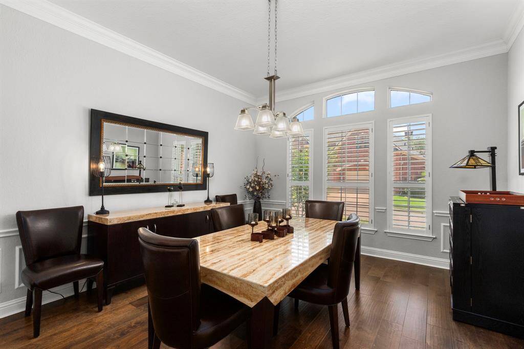 The formal dining room offers wood flooring, high ceilings, deep crown molding and a designer light fixture. The wall of arched plantation shuttered windows with transoms offer views of the pretty front lawn. This room is large and can easily accommodate a large dining table and seating with plenty of room leftover for a buffet and serving console. A wonderful place for formal dinners and celebrations.
