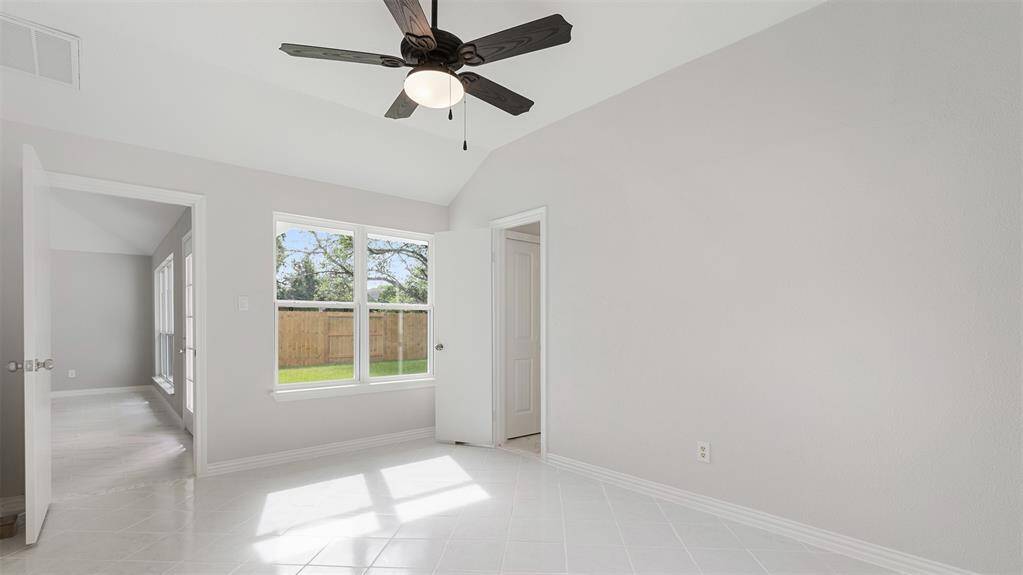 Bright, spacious room with neutral walls and tile flooring. Features a ceiling fan, large window with a view of a fenced yard.