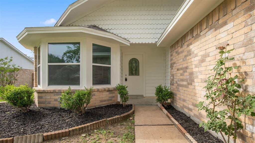 Charming home entrance with a brick exterior and a welcoming walkway. Features a bay window and landscaped garden beds, adding curb appeal.