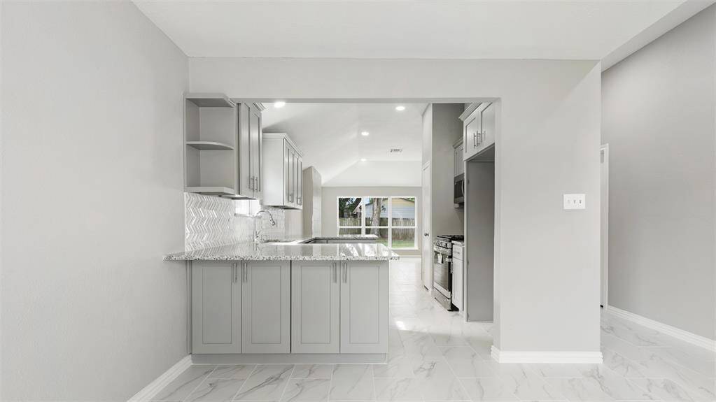 Modern kitchen with sleek gray cabinetry, granite countertops, and a stylish backsplash. Open layout with plenty of natural light and stainless steel appliances.
