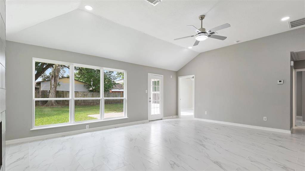 This spacious living room features high ceilings, a ceiling fan, and large windows offering plenty of natural light with views of the backyard. The room is finished with sleek, light-colored flooring and neutral walls, providing a modern, open feel.