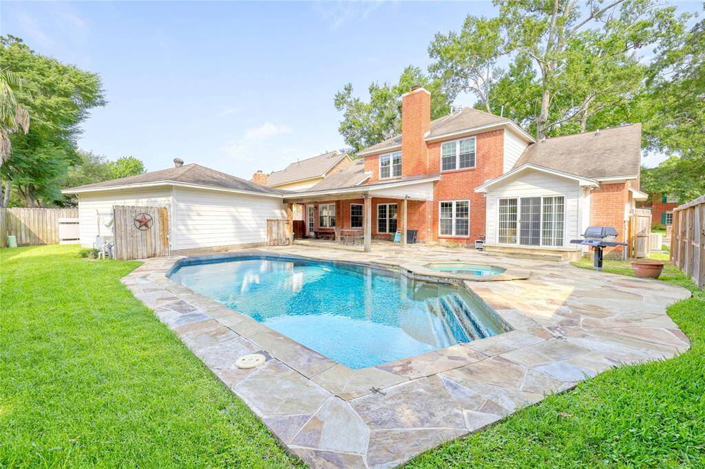A beautifully maintained backyard featuring a sparkling in-ground pool with an attached spa, all surrounded by a flagstone patio.