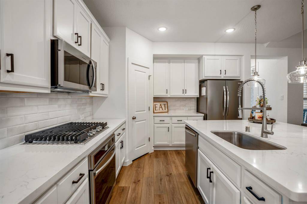 From this angle, you can get a closer look at the built-in oven with a gas cooktop above, surrounded by ample cabinetry that perfectly complements the sleek design of the kitchen. The large corner pantry offers excellent storage, while the fridge is neatly integrated into the cabinetry. To the right of the fridge, a hallway leads to the back door and the primary suite, offering a private retreat just beyond the kitchen.