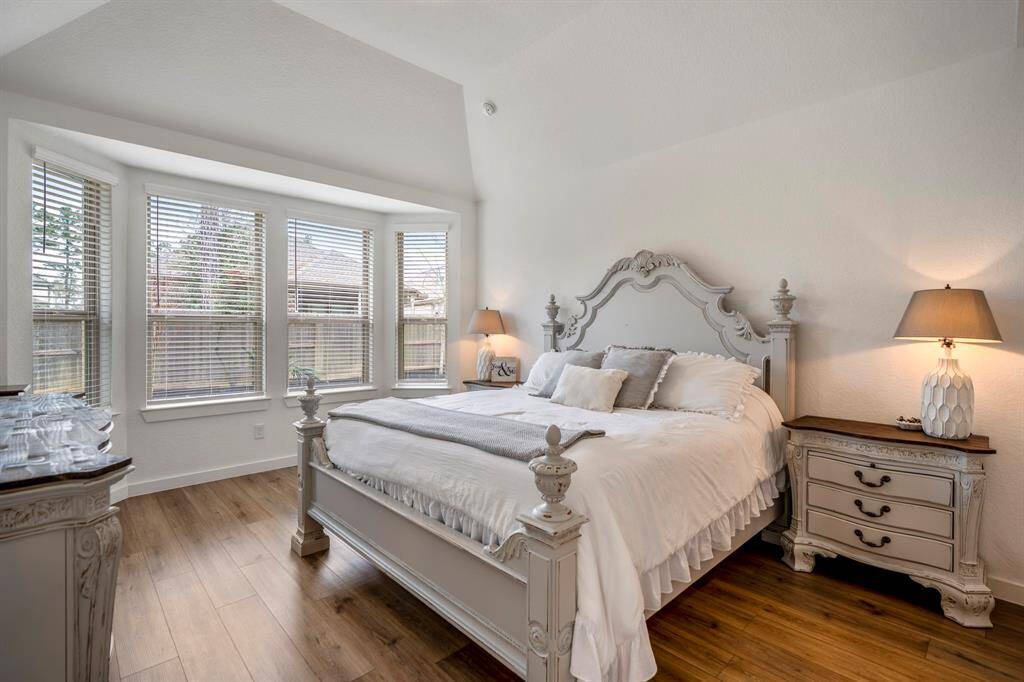 This view of the primary suite highlights the charming bay windows, which create a cozy nook perfect for enjoying natural light and scenic views. The vaulted ceilings continue to enhance the space, making the room feel even more open and inviting. The warm luxury vinyl plank flooring adds a touch of elegance to this tranquil retreat.