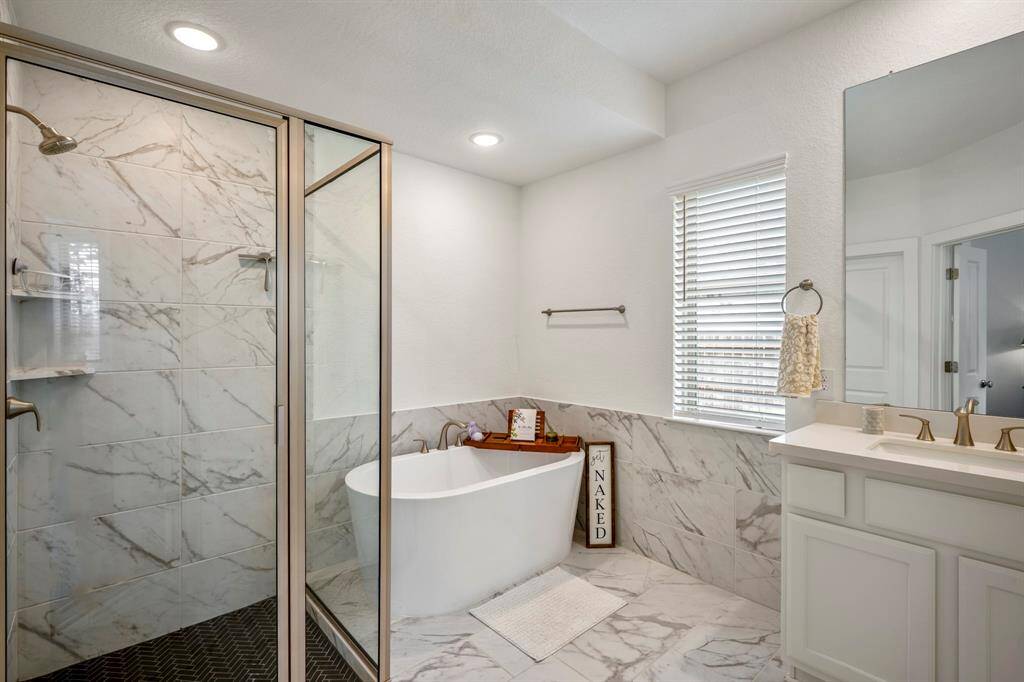Entering the primary bathroom, you'll find a spacious and serene layout. To the left, a separate tile shower with a glass enclosure offers a sleek and modern design, while a freestanding soaking tub, positioned next to a window, creates the perfect spot for relaxation. To the right, dual sinks provide ample counter space, adding both convenience and style to the room.