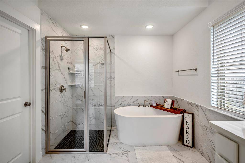 This closer view of the primary bathroom showcases the elegant tile work around the freestanding soaking tub, positioned by a window for a tranquil atmosphere. The clean lines and modern design of the space create a luxurious feel. To the left, the doorway leads to the private potty closet, offering added privacy and convenience.