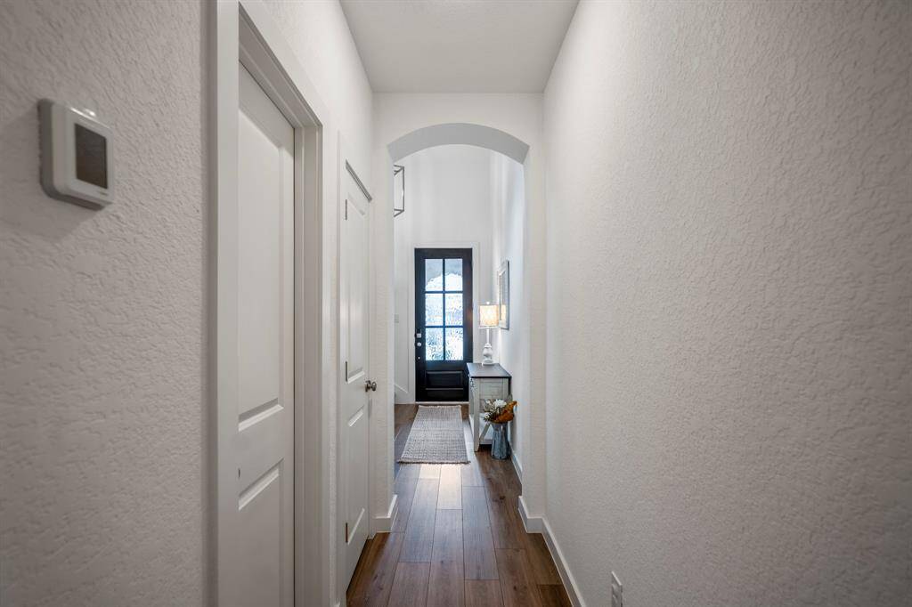 As you move back toward the front of the home, this view captures the hallway between the living room and foyer, nestled beneath the staircase landing. To the left, you'll notice two convenient doors—one leads to the half bath, while the other opens to a coat closet, offering additional storage and functionality. The arched doorways add a touch of elegance to the space.