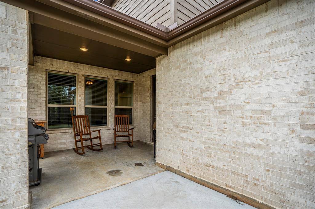 Standing on the patio extension, this view looks back at the covered porch area, where you can appreciate the thoughtful design, including the gutters along the roofline overhead. The extended patio offers extra space for outdoor activities, and the covered porch provides shelter while allowing you to enjoy the backyard and the view.