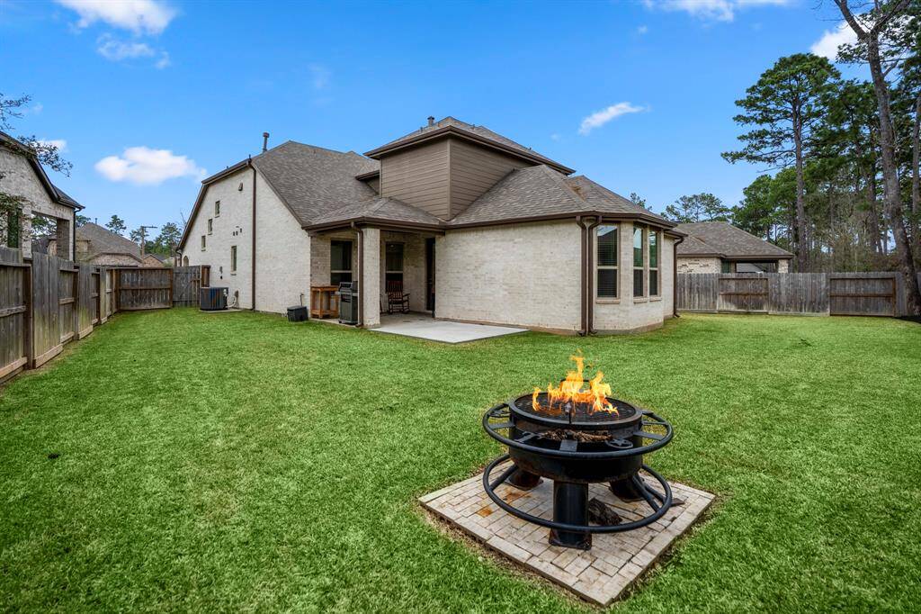 Moving further back behind the firepit, this wide view of the yard showcases the full expanse of the space, with the home in the distance as a beautiful backdrop. The generous yard offers plenty of room for play, gardening, or future outdoor projects, all while providing a peaceful and private setting. The firepit area adds a cozy focal point to this expansive outdoor retreat.