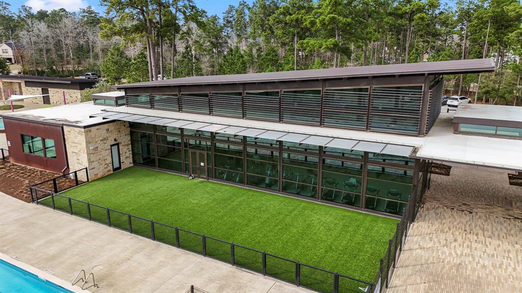 This close-up shot of one of the amenities center buildings in The Woodlands Hills showcases the architectural design and inviting atmosphere. The structure seamlessly blends with the surrounding greenery, offering residents a space for recreation and relaxation. With large windows and modern features, it stands as a central hub for community events and activities, making it a focal point for residents who enjoy both indoor and outdoor amenities.