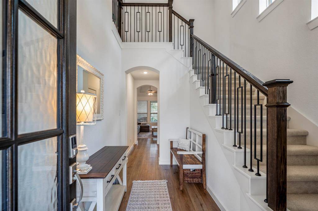 Step inside to a grand foyer featuring soaring ceilings and an elegant staircase to the right. Through the arched entryway ahead, the living room awaits, offering an open and inviting space. Thoughtfully designed, a discreetly placed half bath is tucked beneath the stairs for added convenience.