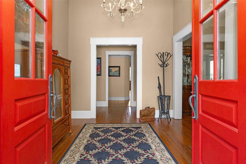 Inside the double red doors is a formal entryway showcasing a beautiful chandelier and original wood flooring.