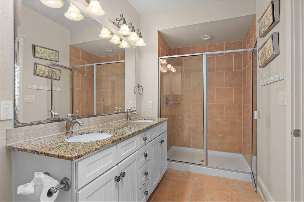 Indulge in the luxurious primary bathroom, featuring a spacious double vanity with ample storage, modern fixtures, and a sleek, glass-enclosed shower.