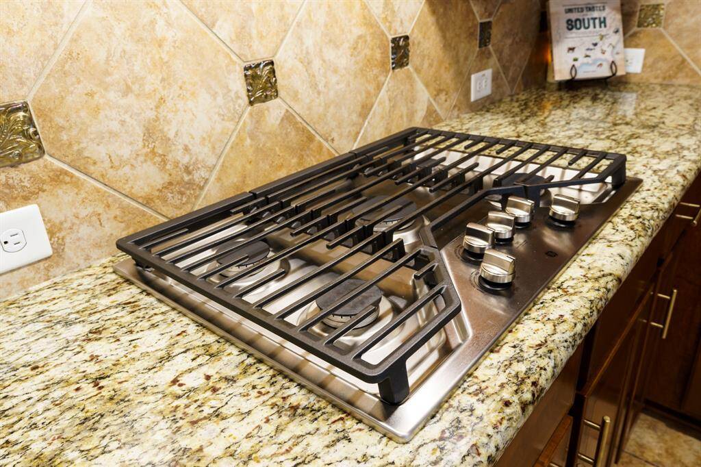 Modern kitchen with a sleek five burner gas cooktop on granite countertops and a stylish tiled backsplash.