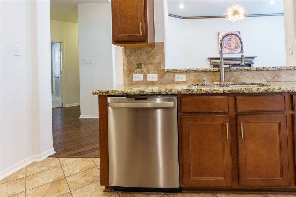 This kitchen features granite countertops, a stainless steel dishwasher, and warm wood cabinetry. It opens to a living area with hardwood floors, creating a seamless flow between spaces.