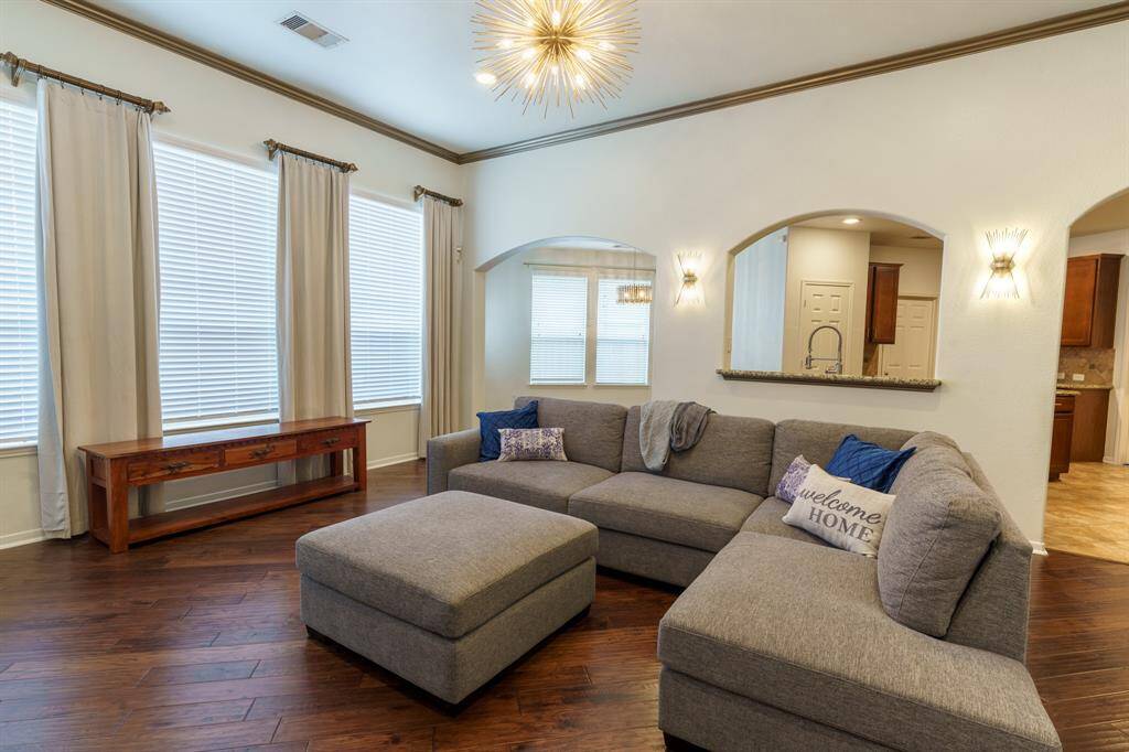 This photo showcases a spacious living area with elegant hardwood flooring, modern lighting fixtures, and an open floor plan. The room features a large, comfortable sectional sofa and connects seamlessly to a dining area and kitchen, creating a warm and inviting atmosphere.