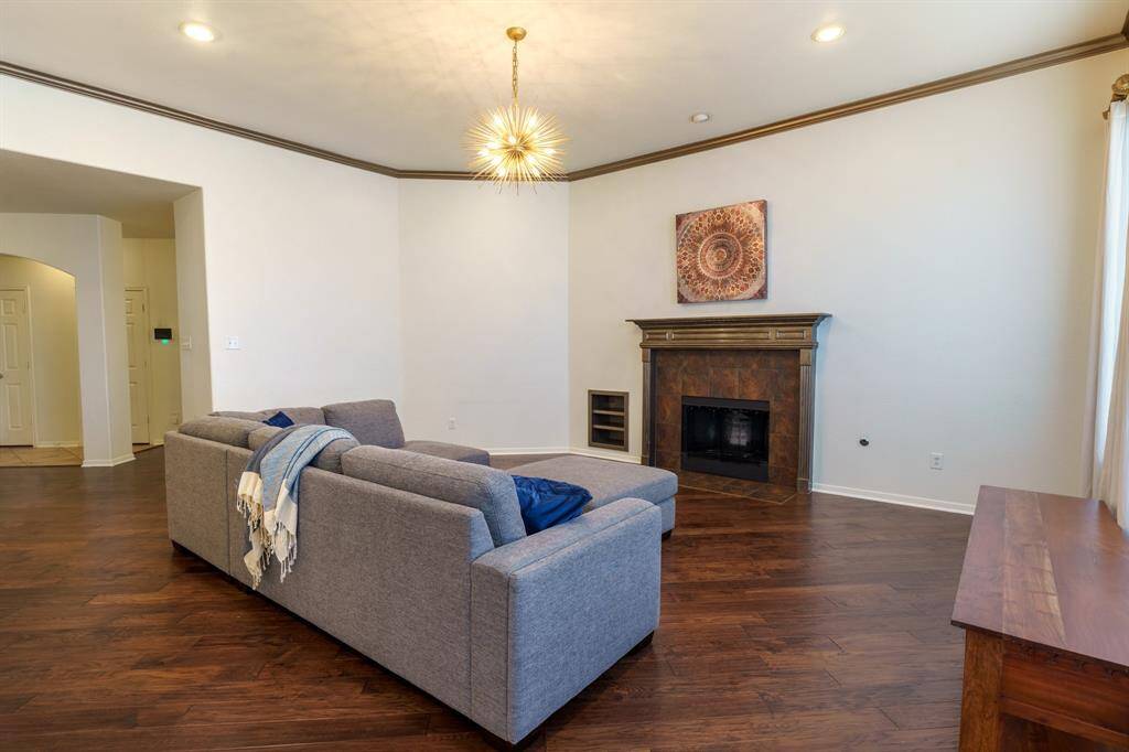 This spacious living room features elegant hardwood flooring, a modern chandelier, and an open layout with arched doorways leading to the kitchen and dining areas. Natural light fills the space, complementing the neutral walls and that will accommodate cozy sectional sofa.