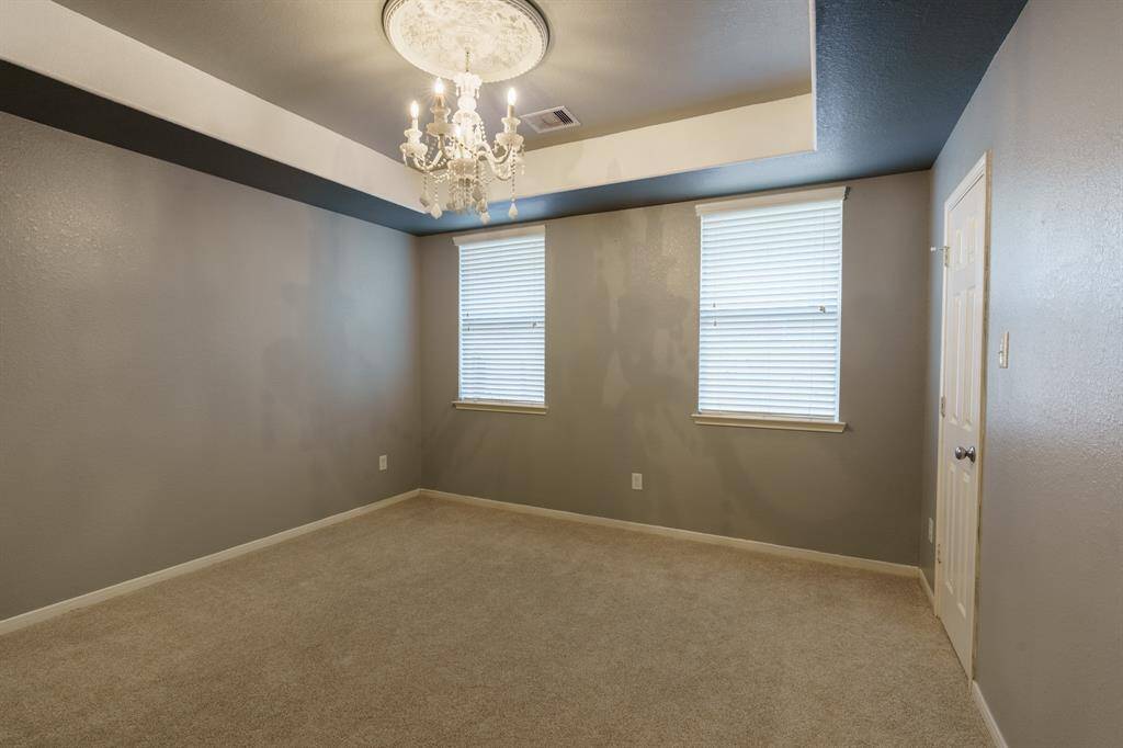 This room features neutral walls, carpeted flooring, and a modern ceiling fan. It has two windows with blinds, offering natural light, and a simple yet elegant tray ceiling design.