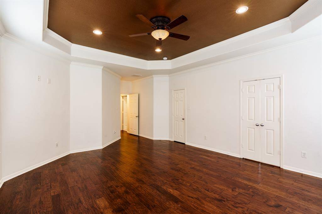 Spacious Primary Bedroom with rich hardwood floors, four large windows, and a stylish tray ceiling featuring recessed lighting and a ceiling fan. The room feels bright and inviting, with a modern, open layout.