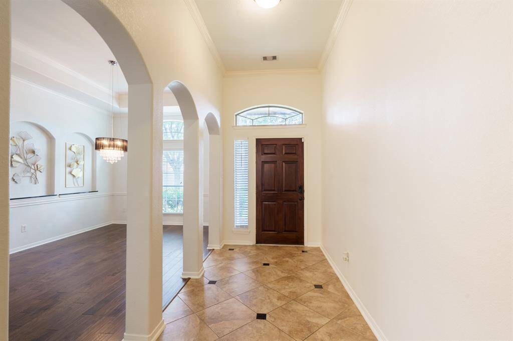 This photo showcases a bright entryway with a dark wood front door, tiled flooring, and arched openings leading to a spacious room with hardwood floors and elegant wall decor.