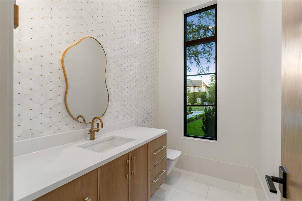 Adjacent to the study, this windowed powder room includes a wall-mounted Toto commode, a large wood vanity, designer tile and coordinating gold-tone hardware.