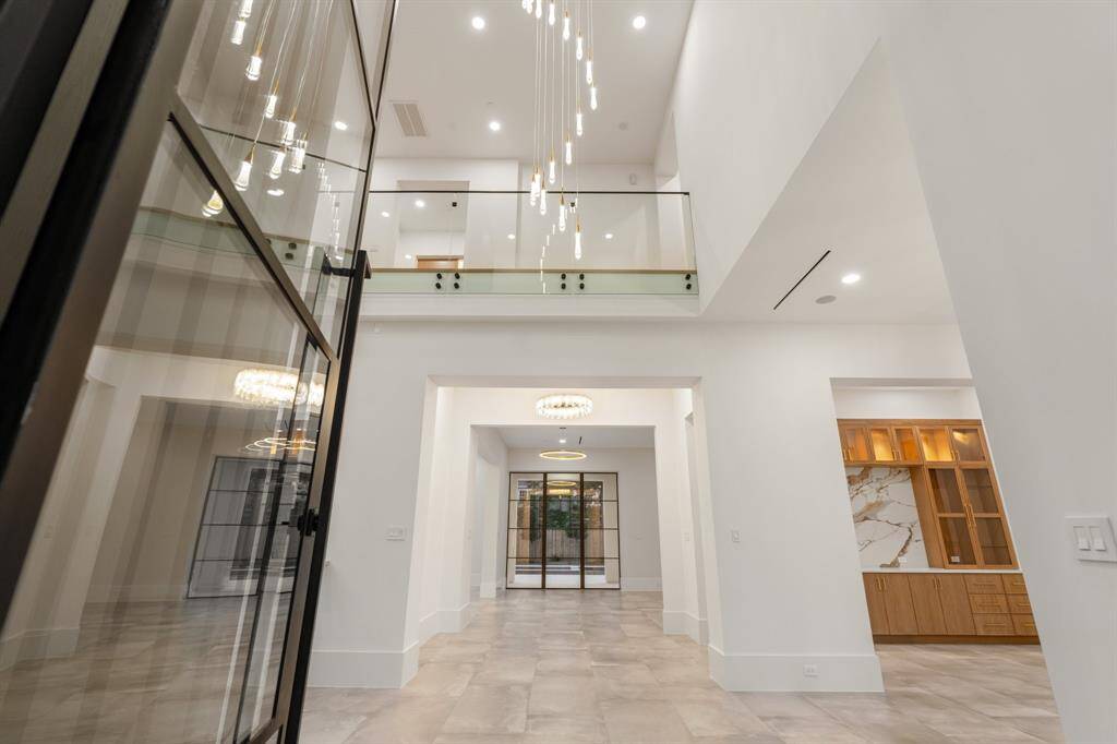 A glass and aluminum entry door welcomes you inside this brand-new 8,982-square-foot Piney Point Village showplace brought to you by Houston Home Builders.