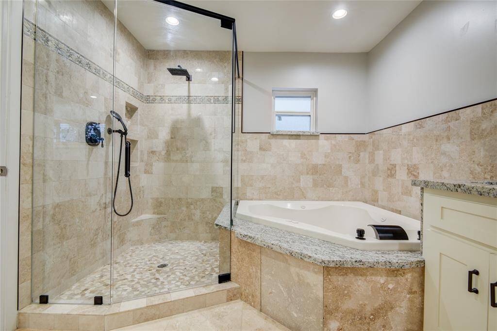Travertine walls tie to the travertine floors, seamless glass shower enclosure, & luxurious jetted tub.