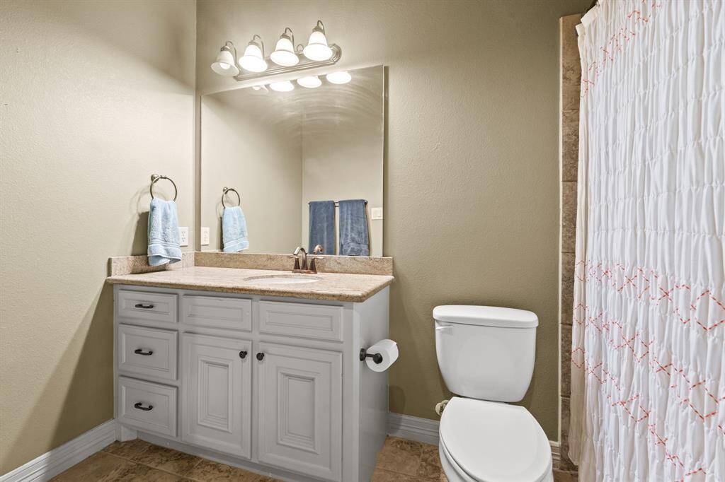 Secondary bathroom with tile floors, granite countertops and backsplash, white cabinetry and a mirror.
